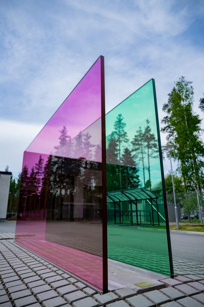 Magentan ja syaanin väriset lasilevyt pystyssä rinnakkain Immolan sotilaskodin pihassa